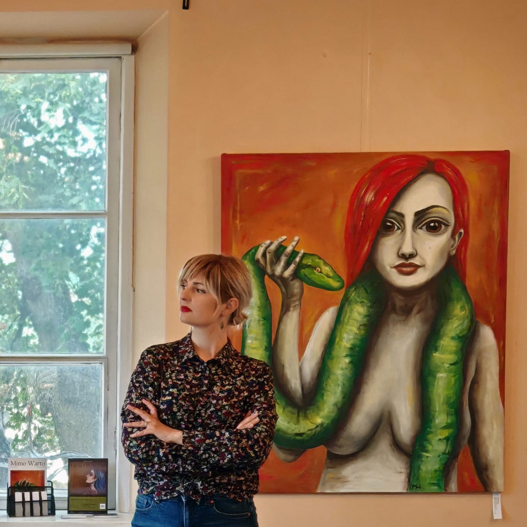 Mimo Warto stands beside her evocative piece 'Know Your Friend,' where the powerful symbolism of the snake intertwines with the figure of a woman.