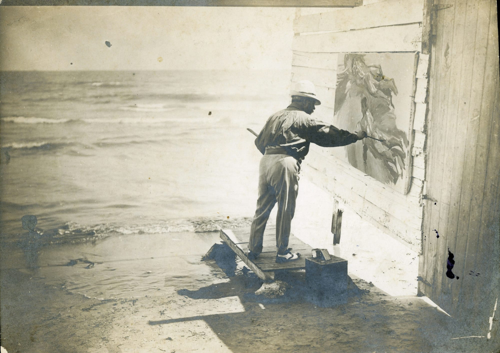 Black-and-white photo of Joaquín Sorolla painting “Boys on the Beach” at the shoreline, 1910.